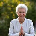 Elena, una mujer sonriente de unos 60 años, meditando en un jardín
